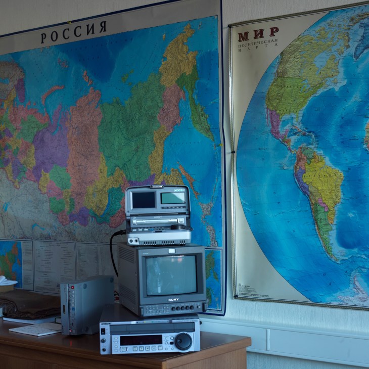 Broadcasting equipment stacked on a desk in front of world maps with Cyrillic text.