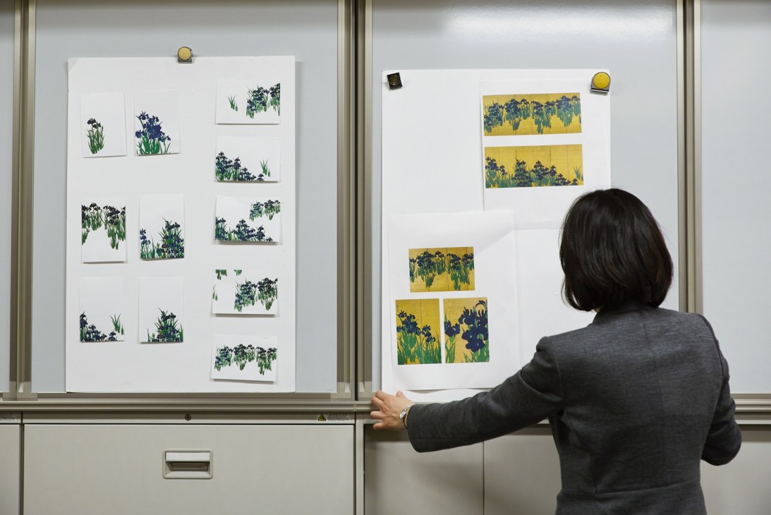 Mamiko Arakawa examines postcard proofs featuring iris designs pinned to display boards.