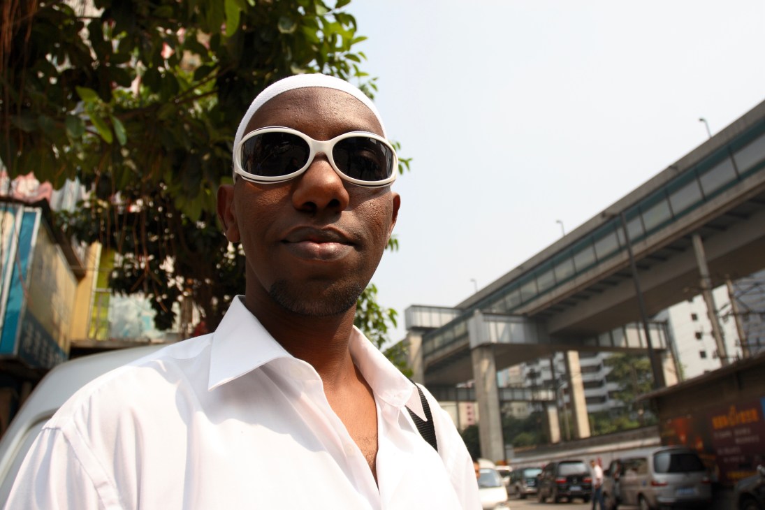 A Somalian man in white sunglasses and white shirt stands on a Guangzhou street.