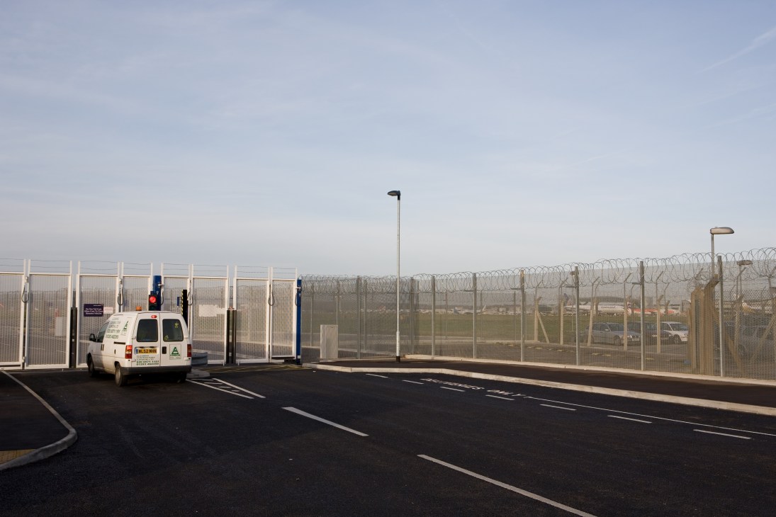 A white police van parked at Gatwick airport's perimeter fence topped with coiled razor wire.