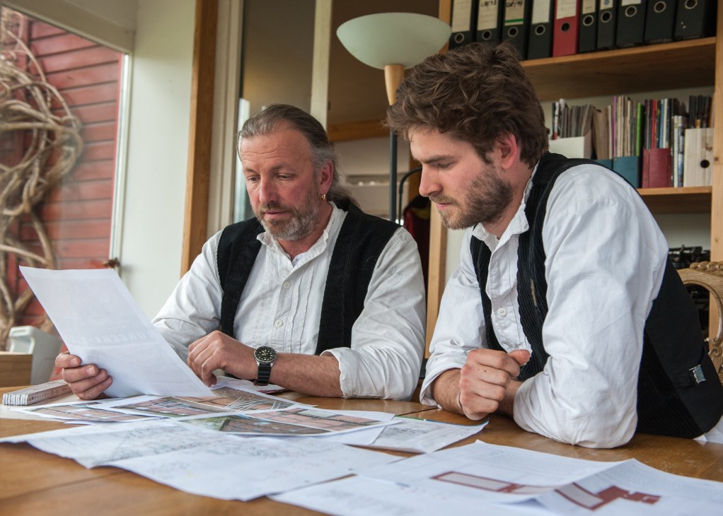 Master carpenter Martin Kottmeier and apprentice Jonas Klann review architectural plans at a wooden desk.