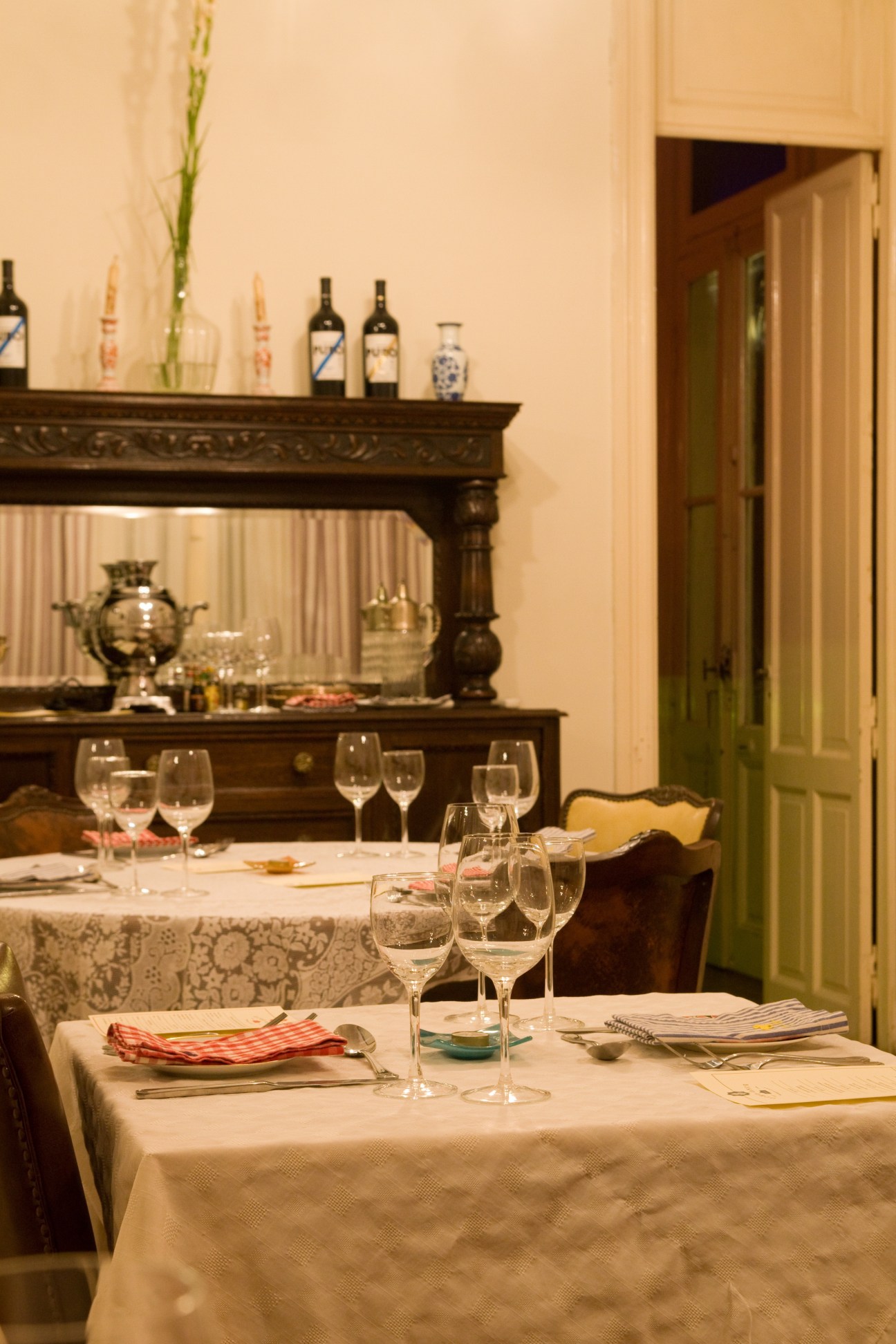 Elegant dining room at Ocho Once restaurant with set tables, fireplace mantel displaying wine bottles, and green door.