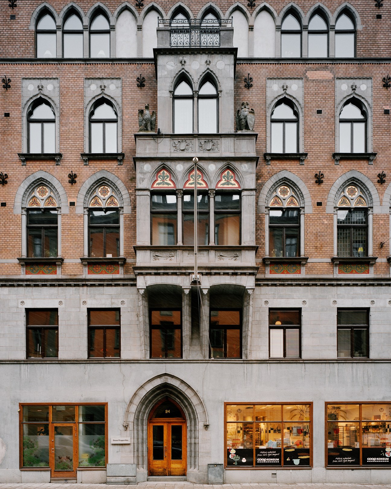 Red brick 19th-century building facade with Gothic arched windows, stone eagle and owl sculptures, and ornamental details.