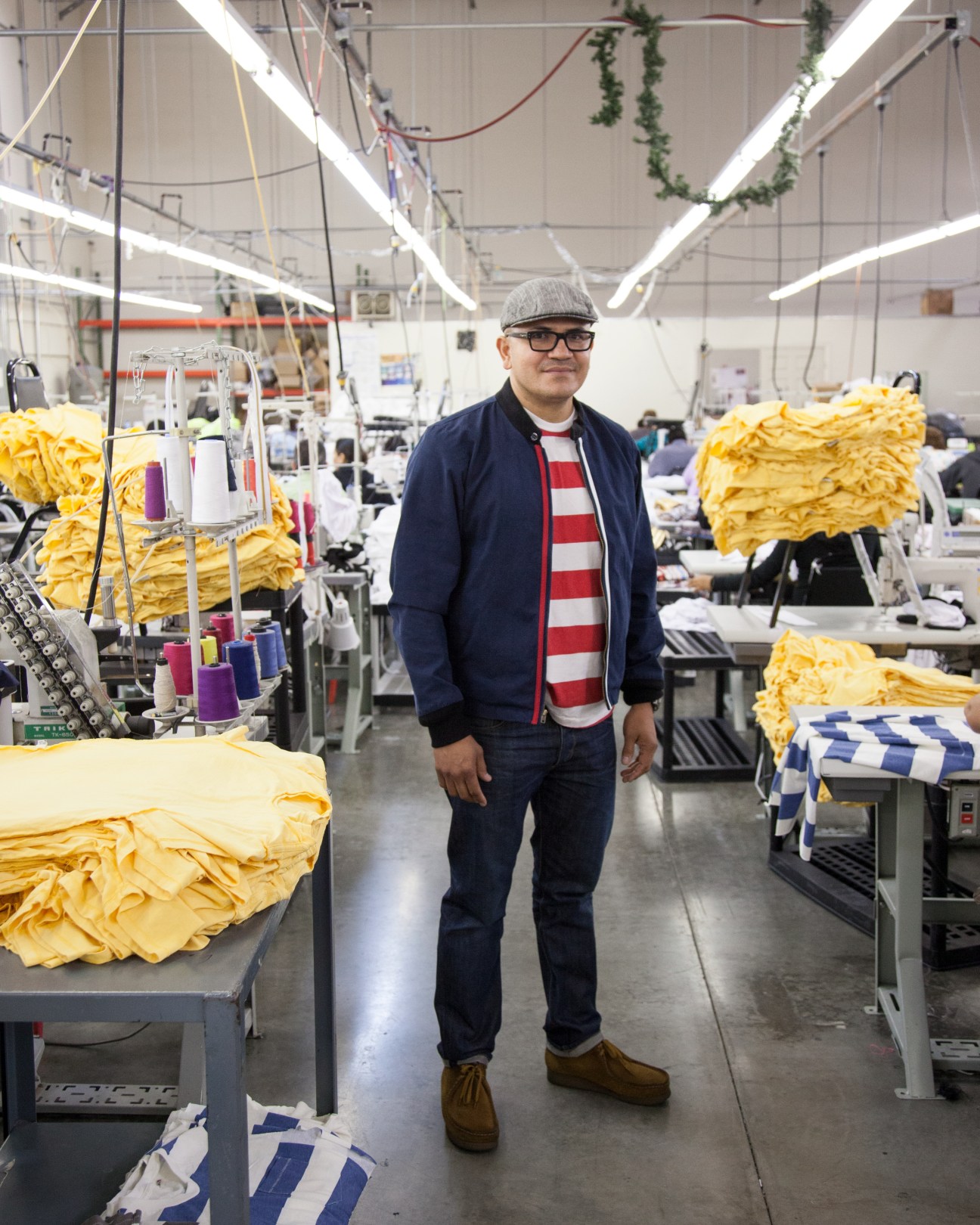 Raul Montero stands in a bright factory floor surrounded by stacks of yellow fabric at Lunas Inc manufacturing facility.