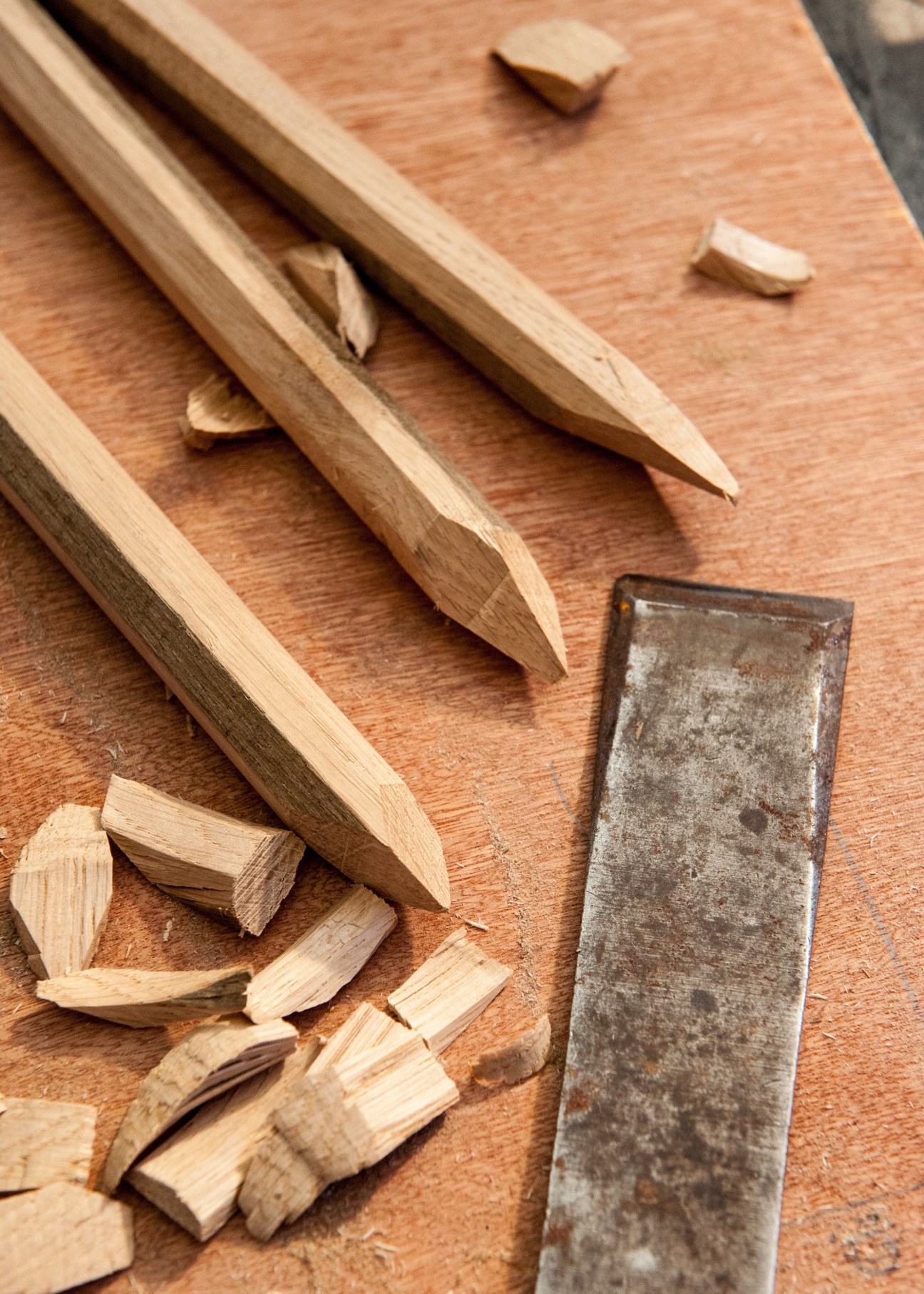 Wooden pegs and lathes with sharpened points arranged on a wooden surface next to a metal tool.