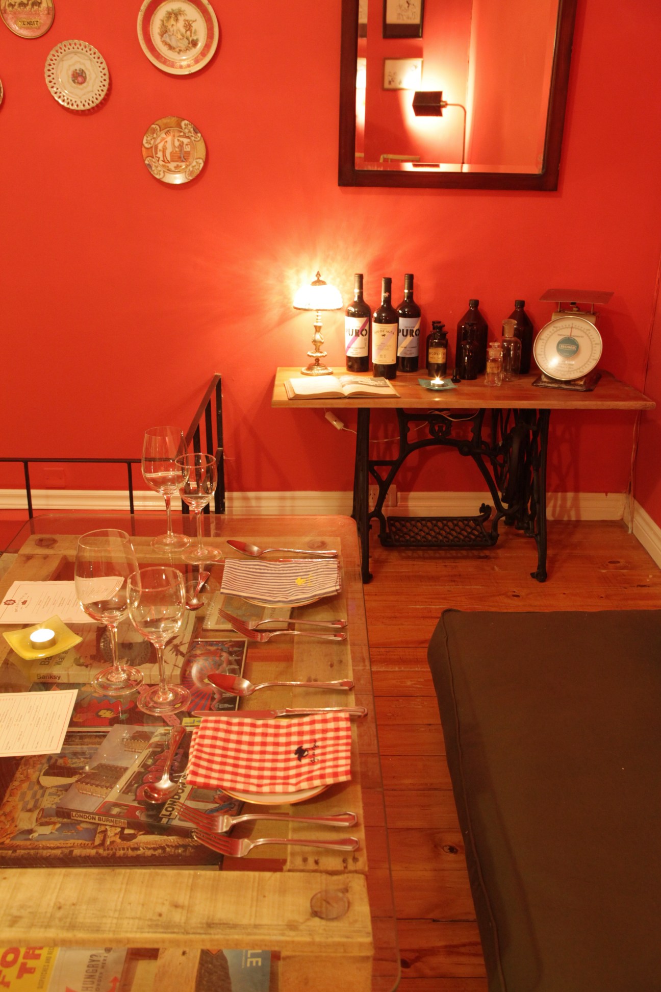 Intimate dining room with vibrant red walls, set table with wine glasses, and decorative plates on the wall.