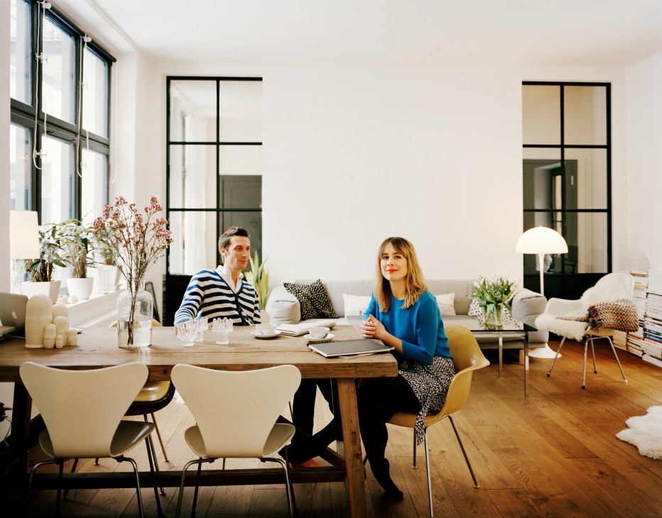 Fashion designer Carin Wester and Thomas Pouverel seated at their dining table in a modern apartment with high ceilings and industrial windows.