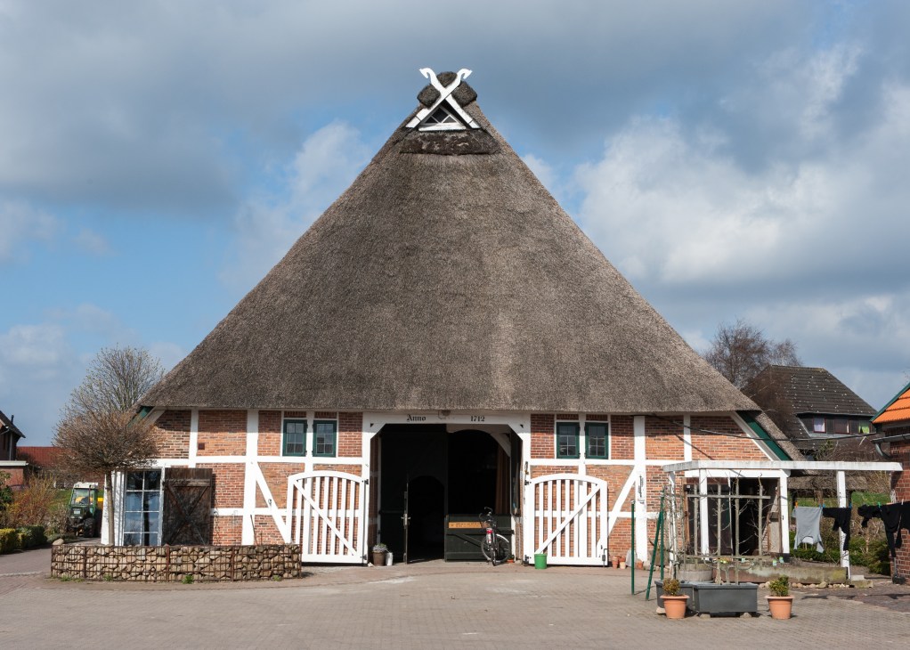 A traditional timber-framed house with thatched roof and white-painted wooden beams on red brick.