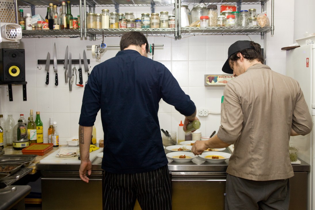 Two chefs apply finishing touches to plated dishes in a kitchen at Ocho Once restaurant.