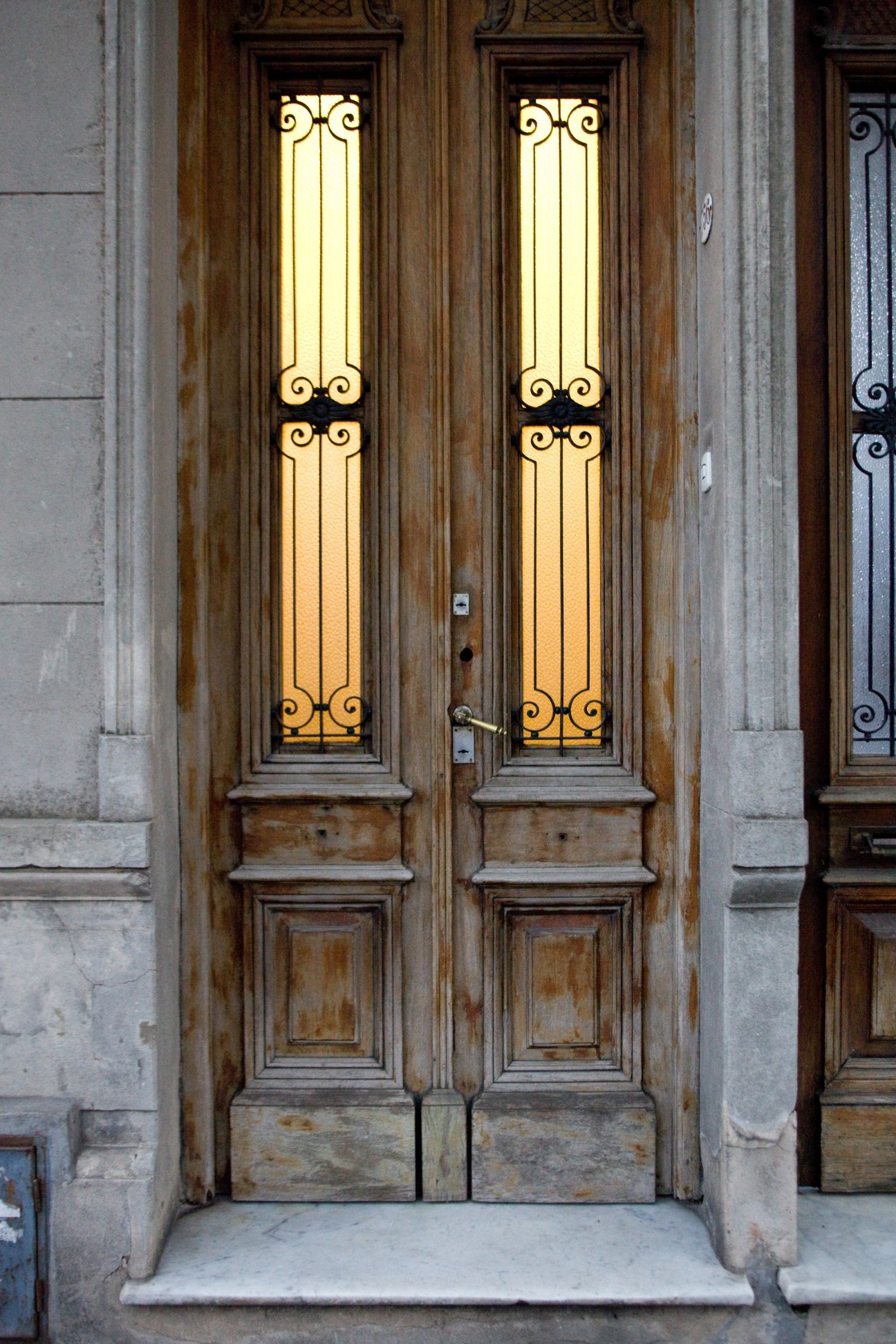 Ornate wooden double doors with illuminated glass panels featuring wrought iron designs on a stone facade.