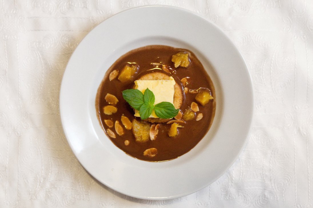 Orange parfait with hot chocolate soup served on a white plate with mint garnish.