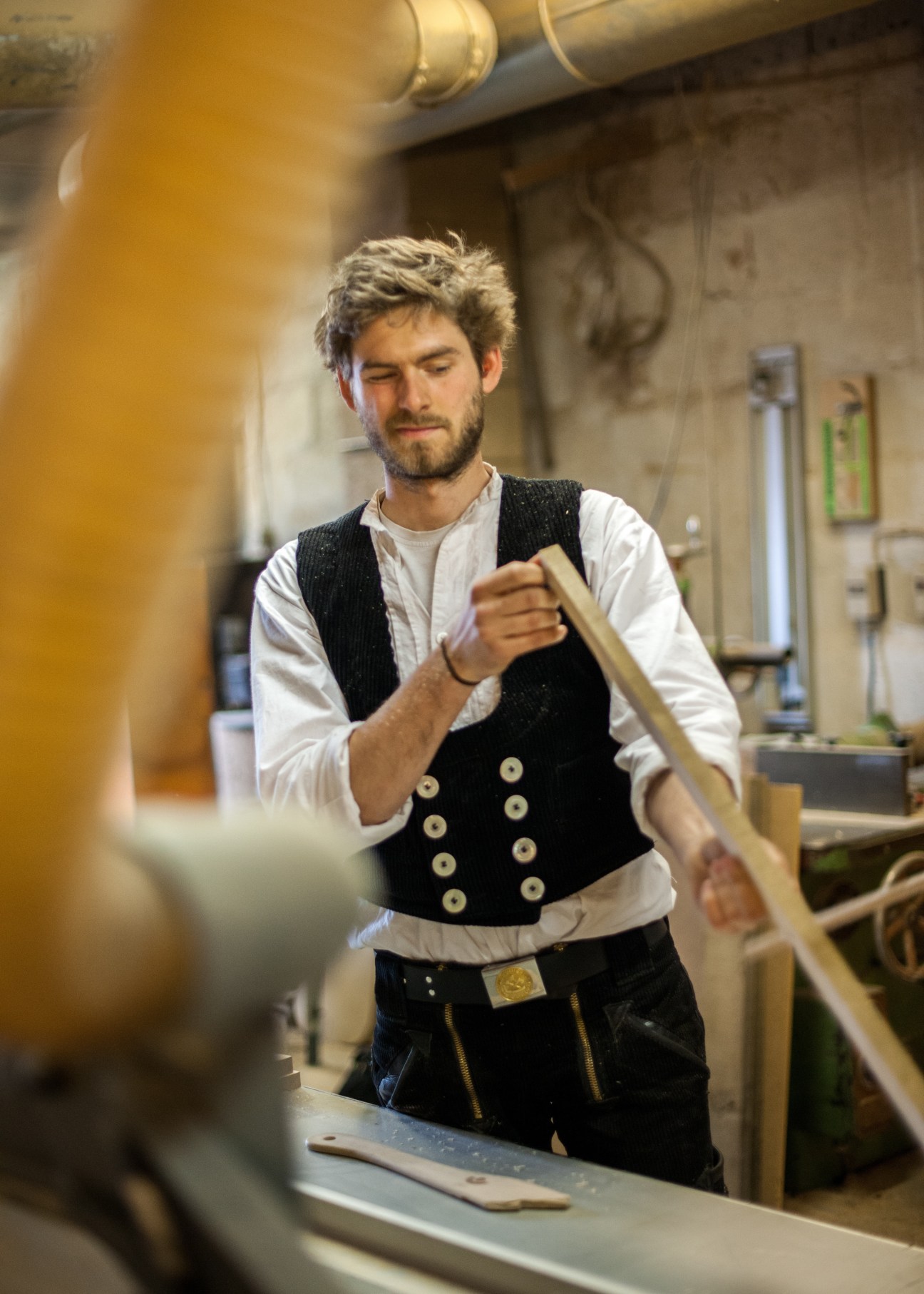 Jonas Klann, a carpenter apprentice, works with a wooden lathe in the FachWerk workshop while wearing traditional German carpenter attire.