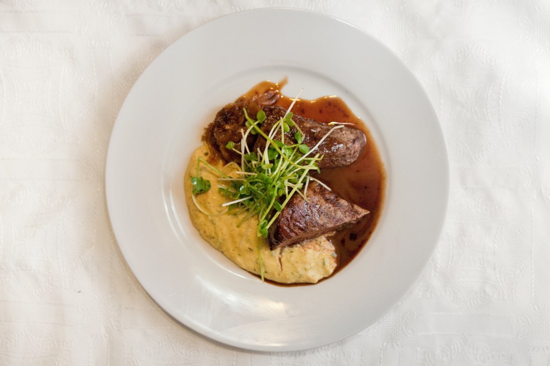 Steak with polenta and cognac sauce plated on white dish with microgreens garnish.