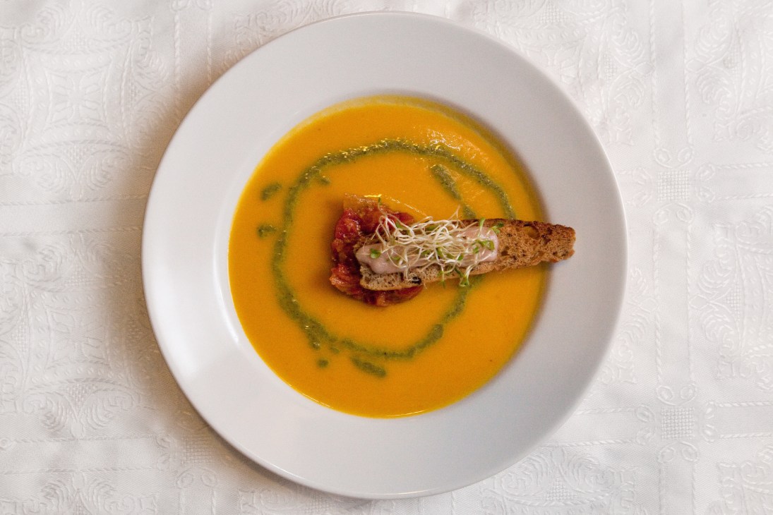 Chilled carrot-and-orange soup with tomato tartar and microgreens garnish in a white bowl.