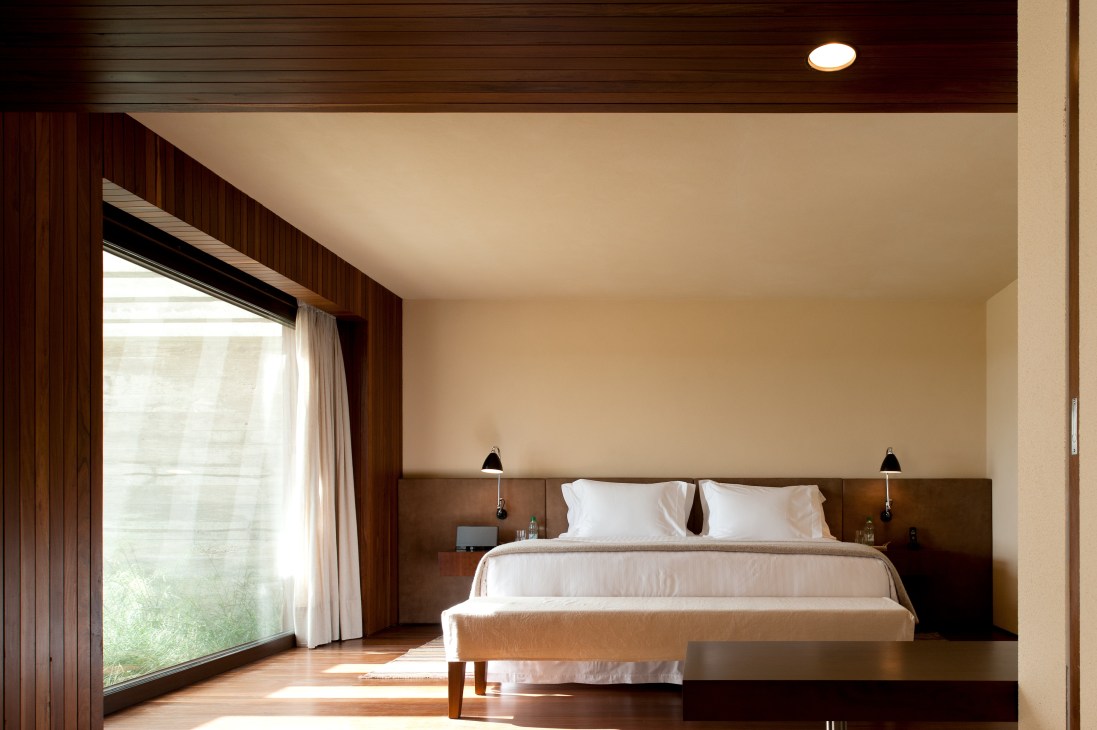 Minimalist bungalow bedroom with wood paneling, large window and neutral furnishings at Las Piedras Fasano.