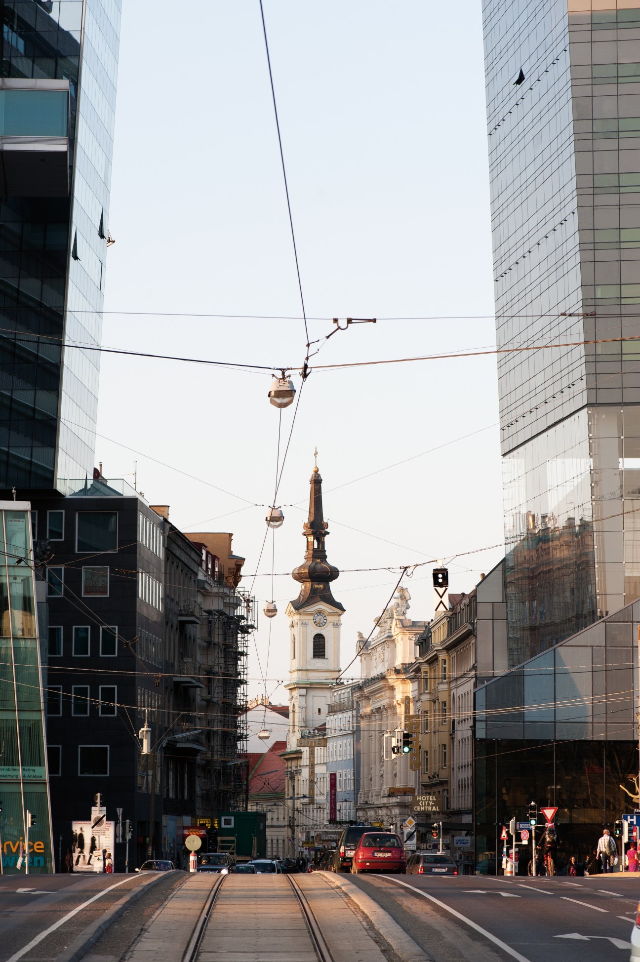 Tramlines running down a Leopoldstadt street lined with modern buildings and a church spire in the distance.