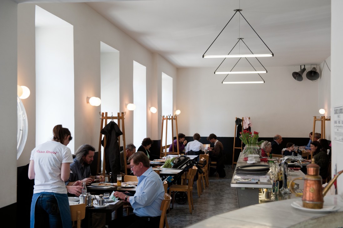 Interior of Pizza Mari restaurant with diners seated at tables and modern geometric pendant lighting.