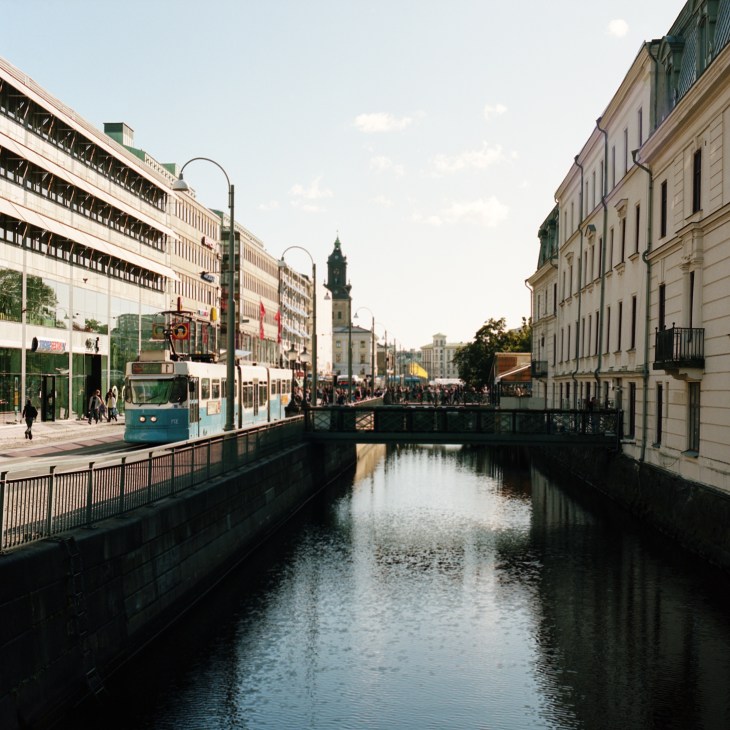 A tram travels along a canal in central Gothenburg, lined with classical buildings and modern structures.