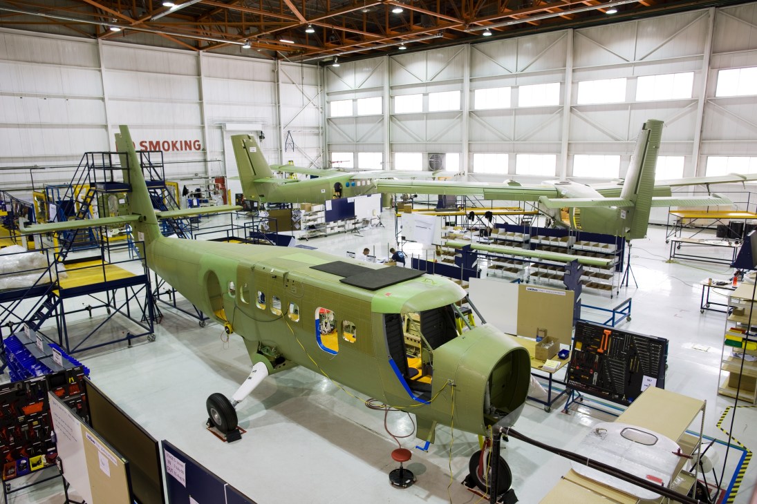 Three Twin Otter aircraft in various stages of assembly inside a large industrial hangar with bright lighting.