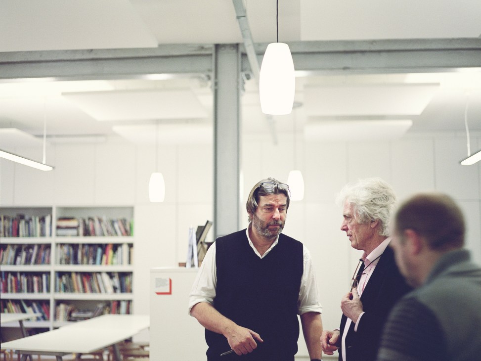 John Thompson, architect, speaks with colleagues in a modern office with bookshelves.