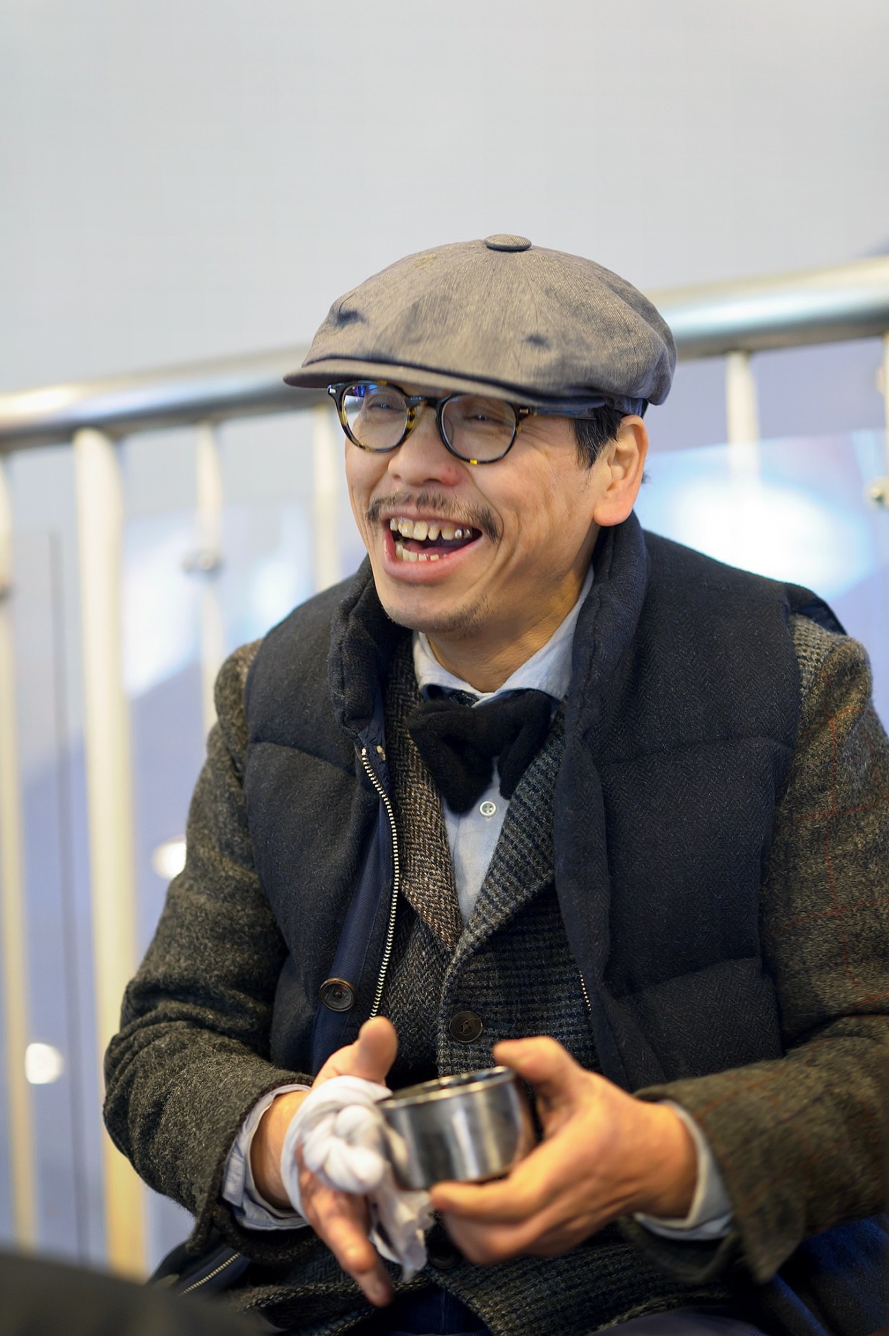 Mikoto Chiba, Tokyo shoeshine operator, wearing glasses, cap and dark jacket, holding a metal container.