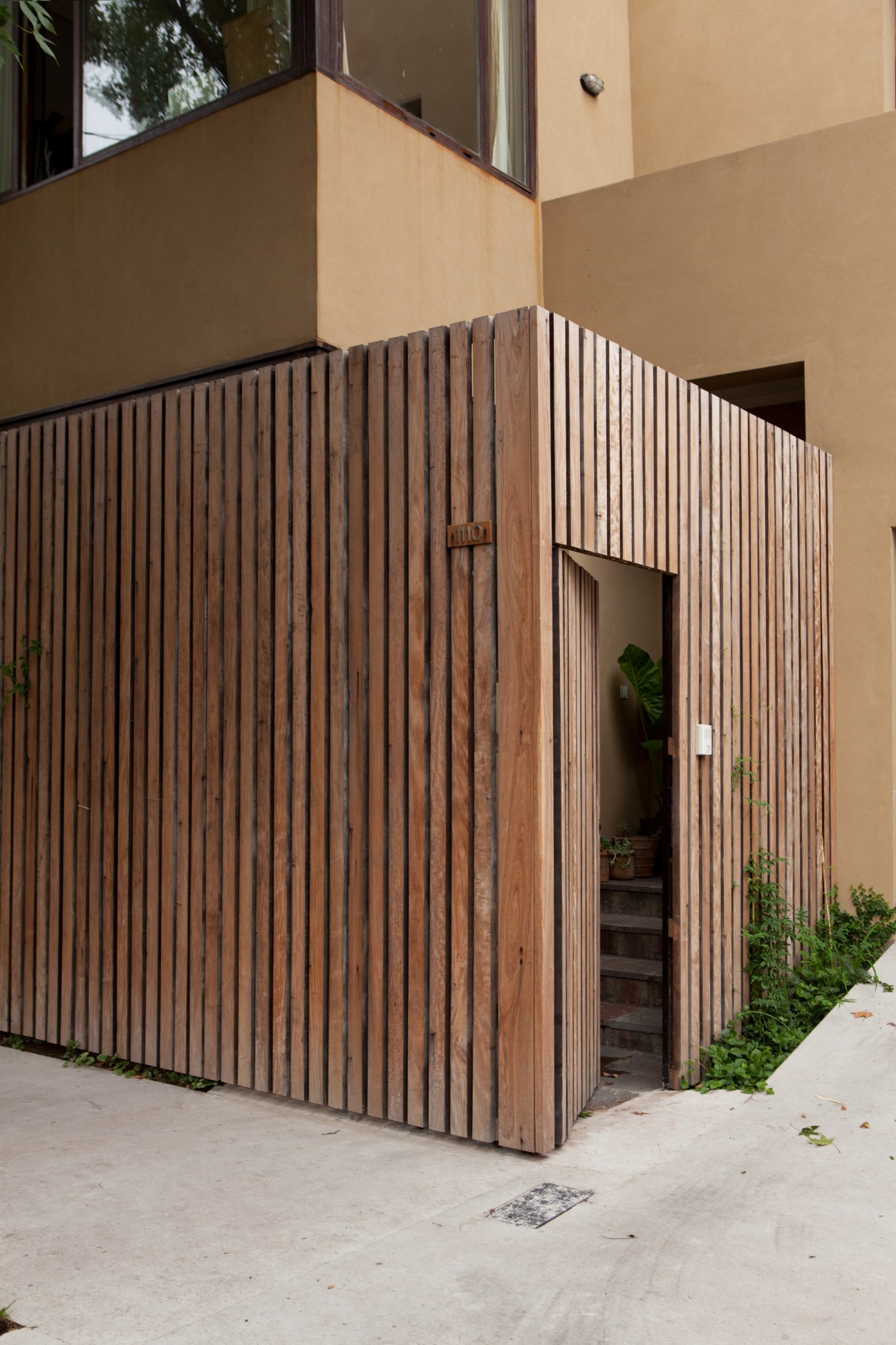 Modern house entrance with vertical wooden slat fence and cut-out door in Buenos Aires