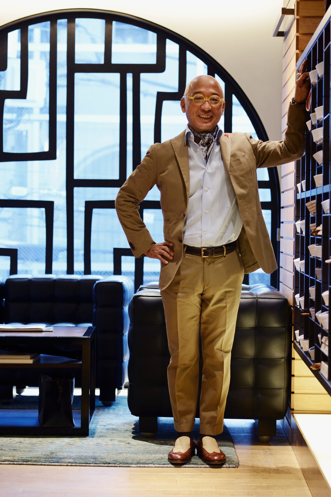 Junji Tajima, owner of Strasburgo, smiling in his Tokyo menswear shop wearing a tan blazer and brown loafers.