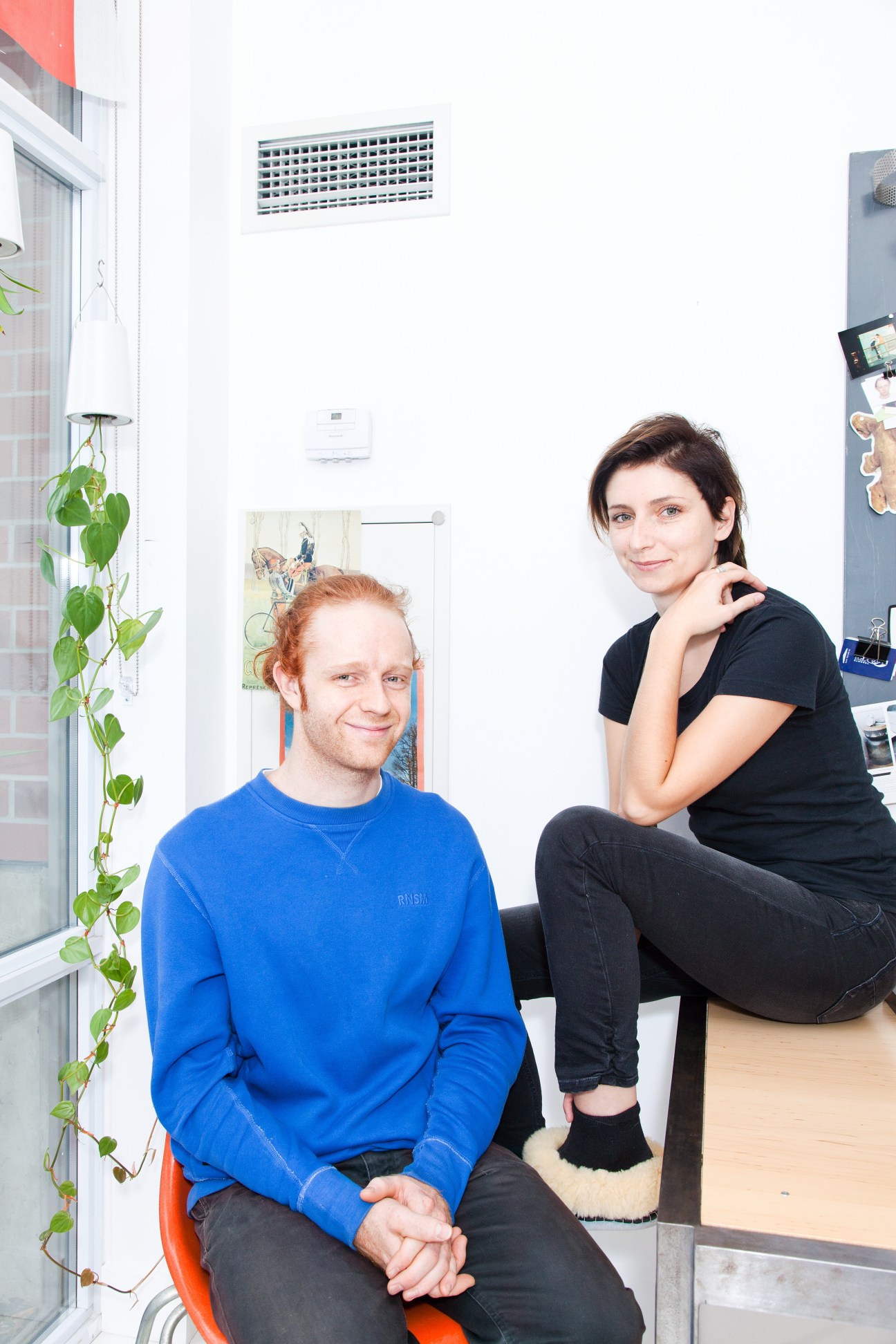Industrial designer Ryan Wilding and photographer Agata Piskunowicz pose in a bright white room with plants and artwork on the walls.