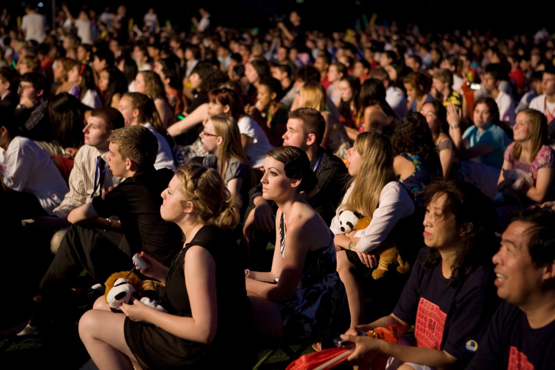 Large crowd of students seated indoors watching an opening ceremony performance at night.