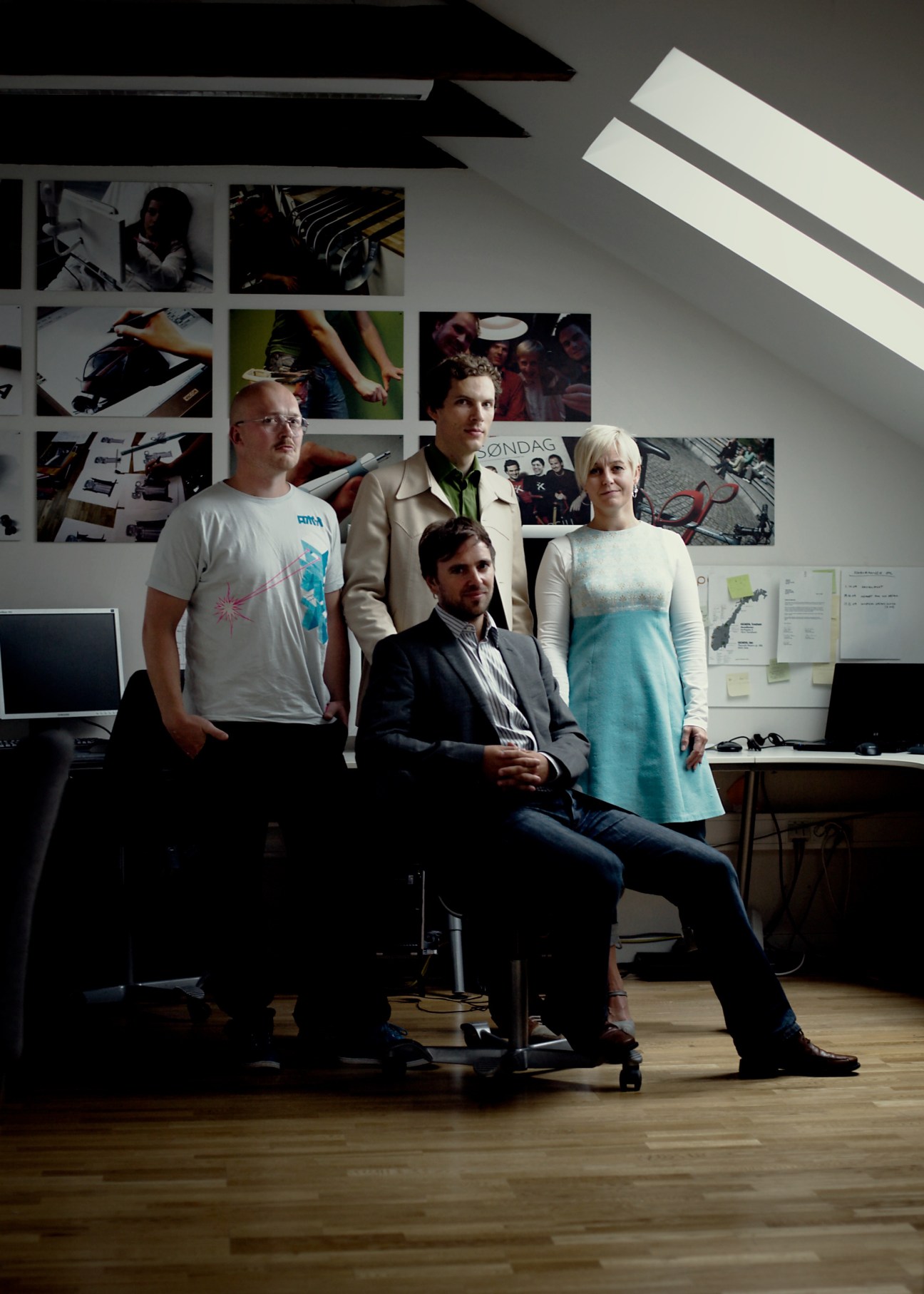 Four designers posing in a studio with portfolio images displayed on the wall behind them.