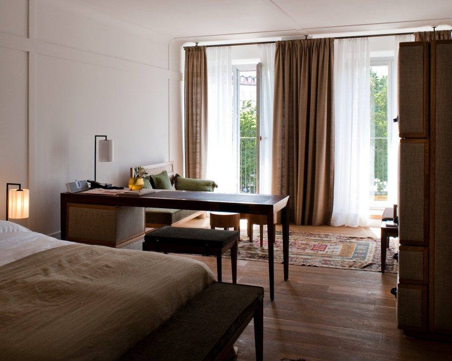 Spacious hotel room at Louis Hotel Munich with bed, desk, and balcony overlooking city.