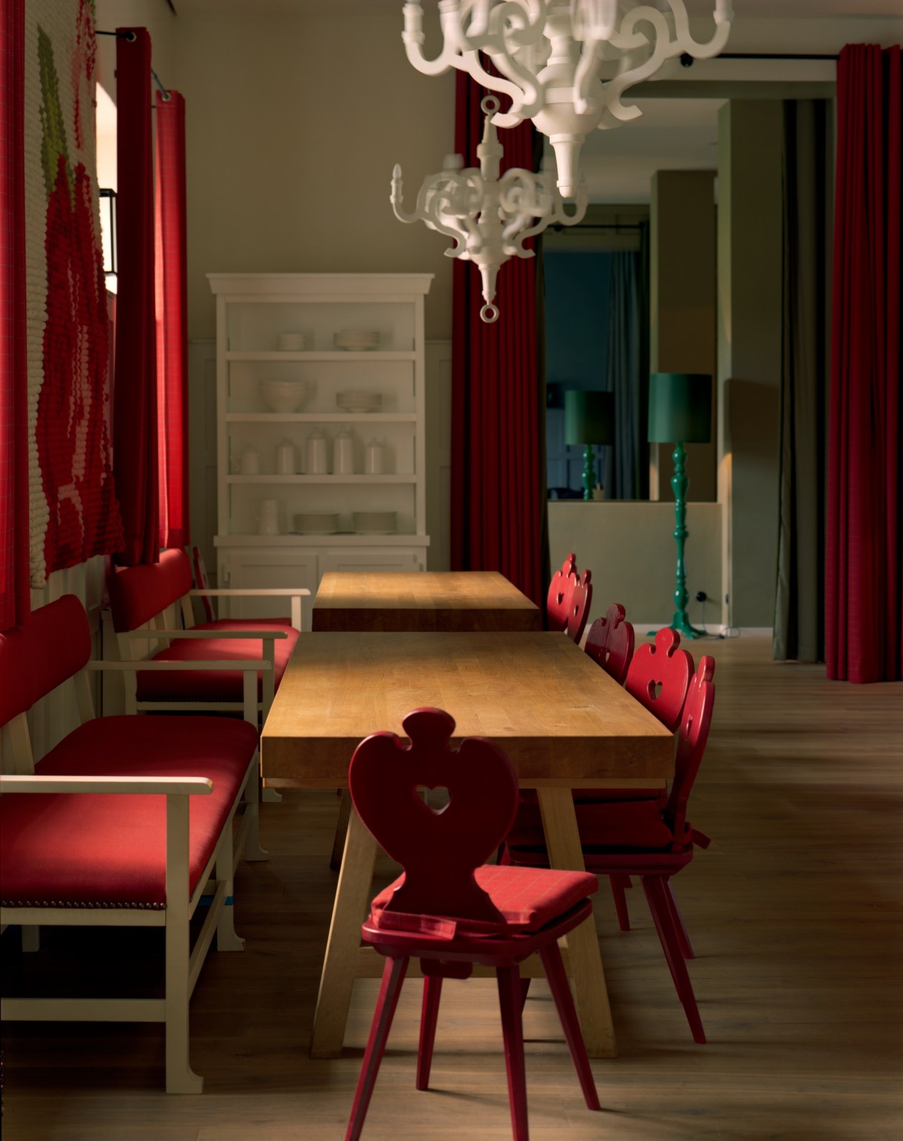 Dining room at Das Kranzbach with wooden tables, red upholstered chairs with heart-shaped backs, white ornamental chandelier, and red curtains.