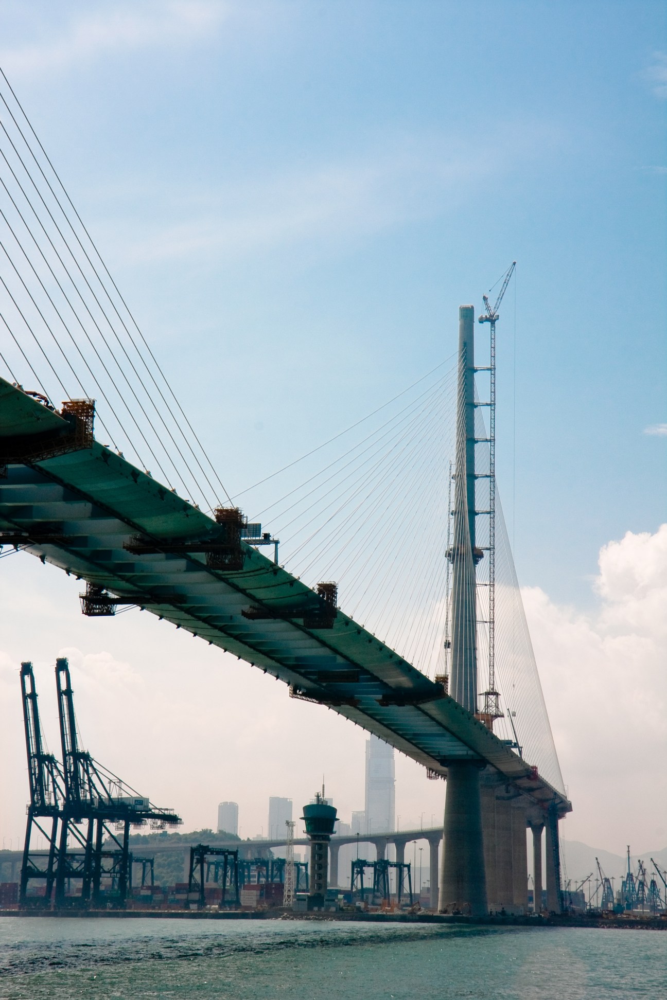 Stonecutters Bridge's cable-stayed towers and deck spanning across Hong Kong's port with industrial structures visible.