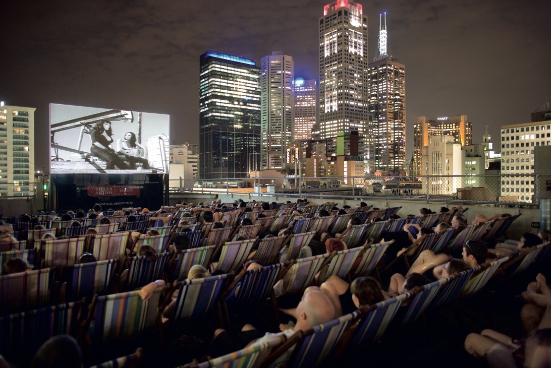 Rooftop Cinema, Melbourne: audiences in striped deck chairs watching a film on an outdoor screen with city skyline at night.