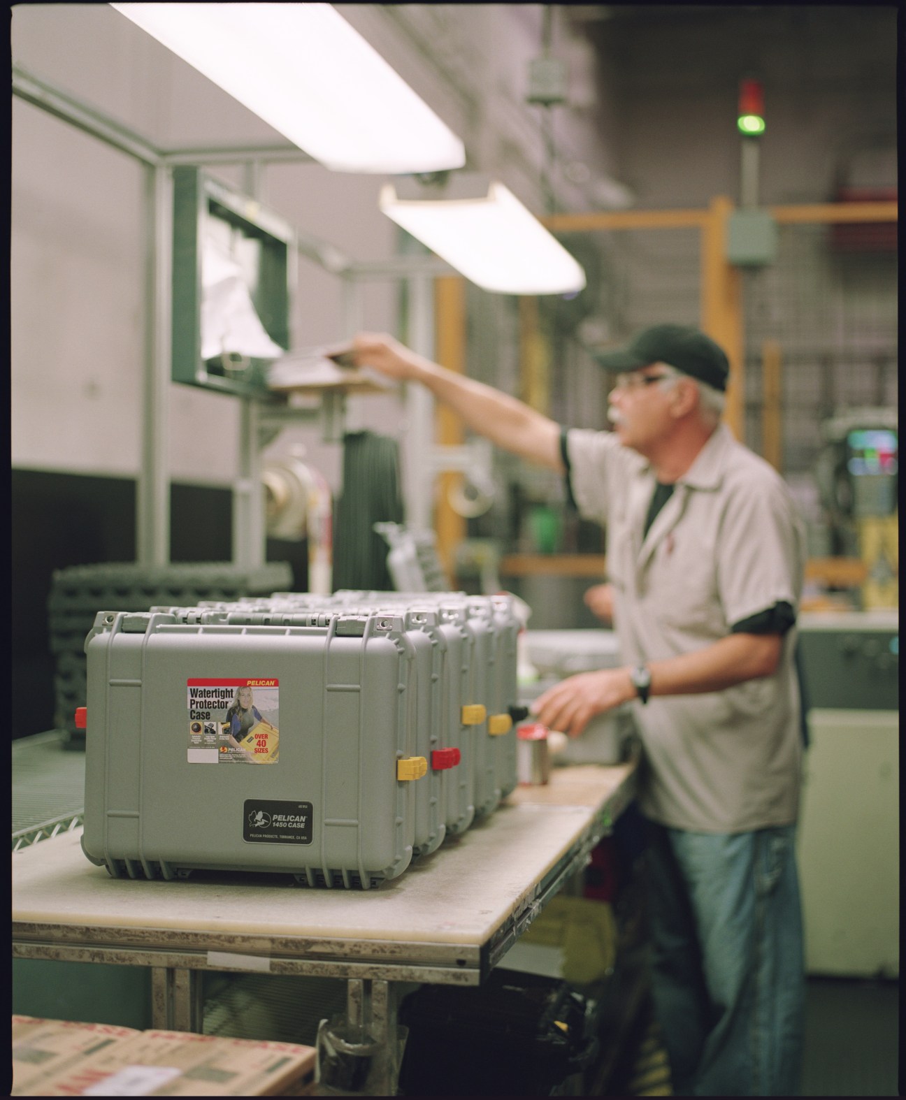 Worker inspecting Pelican protective cases on production line in manufacturing facility.