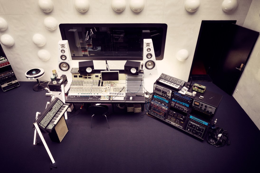 Overhead view of a recording studio workspace with Rupert Neve-designed mixing console, vintage synthesizers, and professional audio equipment.