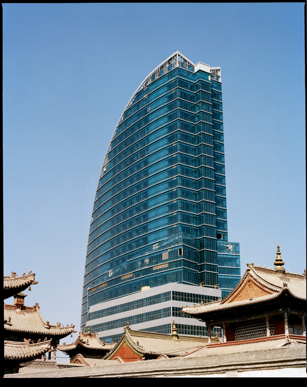 Modern glass and steel skyscraper rising behind traditional Mongolian temple with ornate curved roofs.