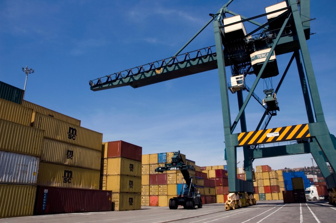 Colorful shipping containers stacked at Barcelona port with a large green cargo crane overhead.