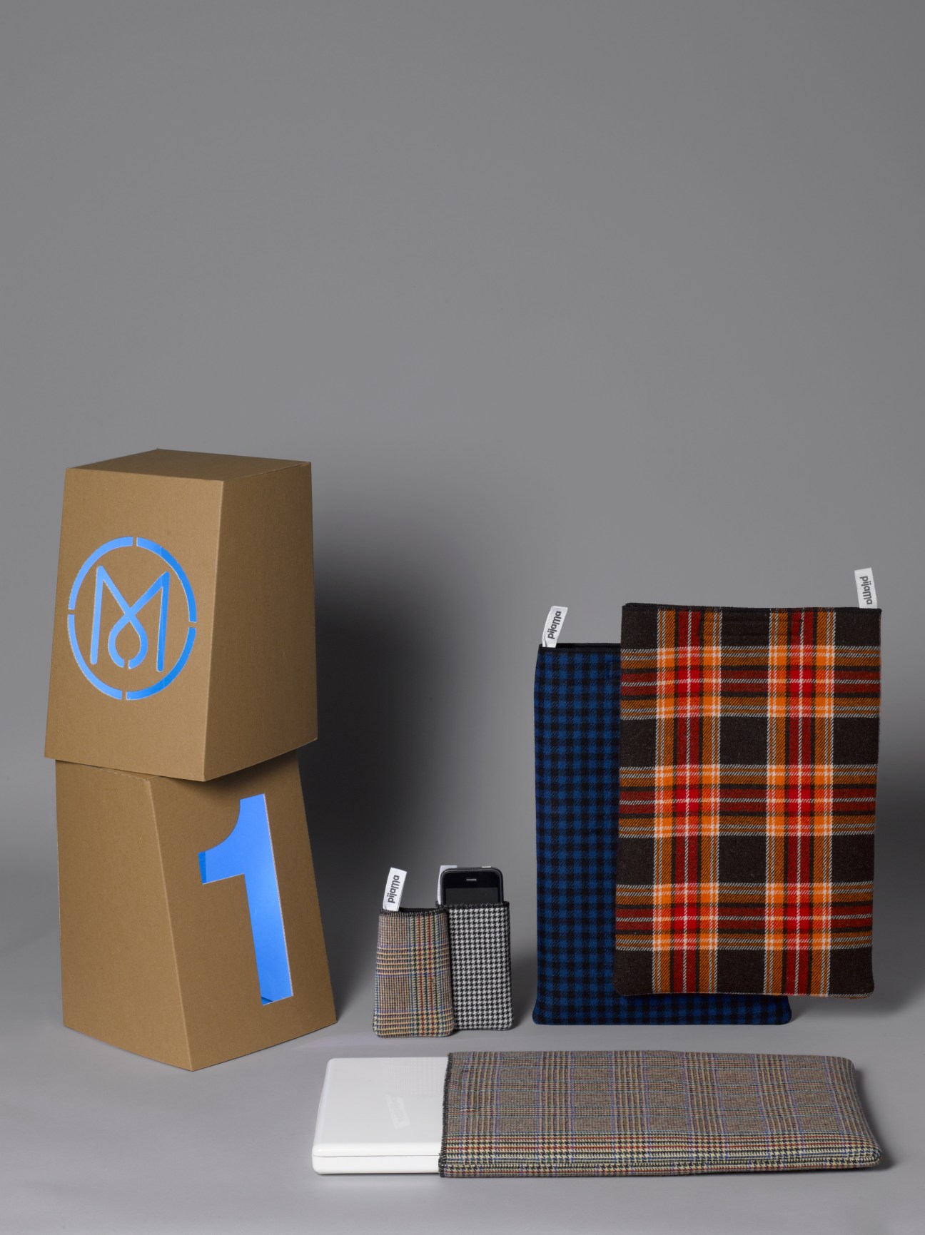Pijama laptop sleeves in tartan and check wool fabrics displayed with branded cardboard packaging.