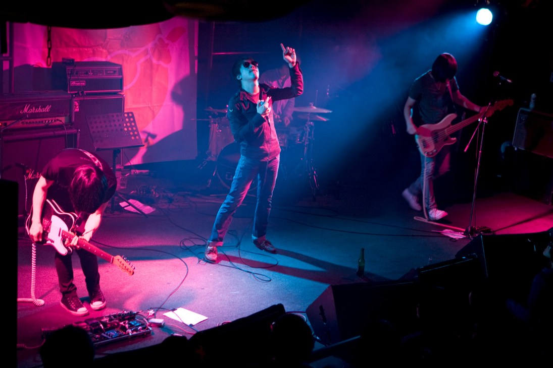 Band 1976 performs on stage at The Wall venue with pink and blue stage lighting.