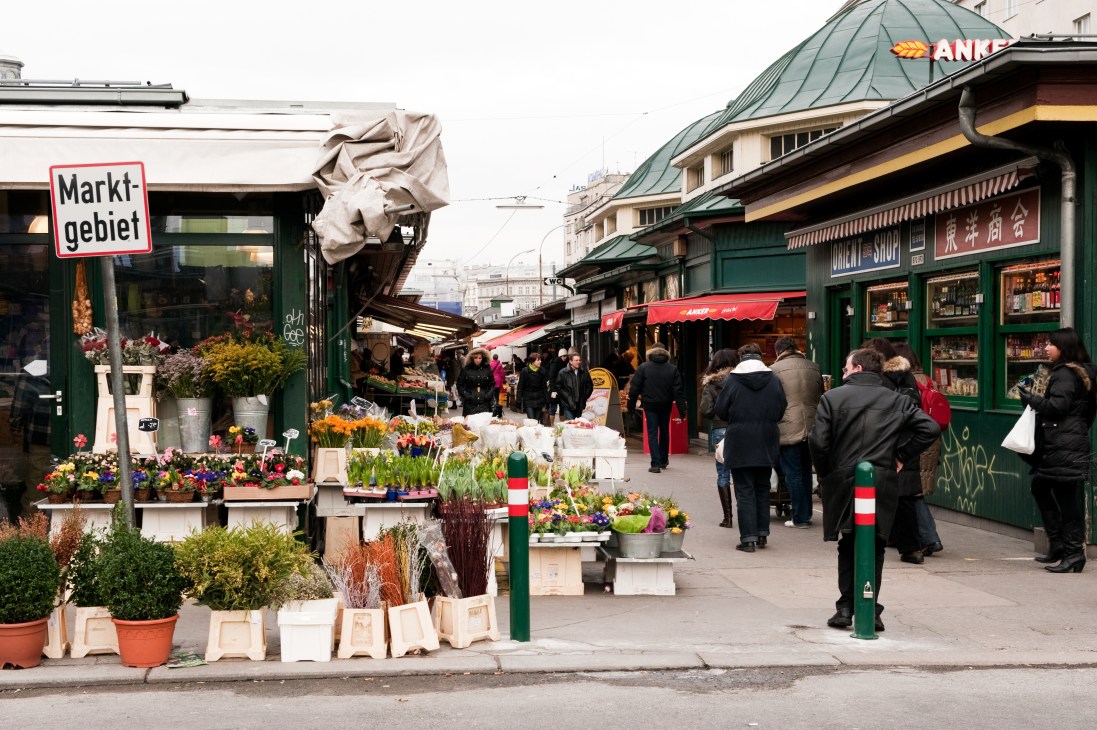 Vienna's Naschmarkt with green market stalls, flower displays, and shoppers under covered walkways.