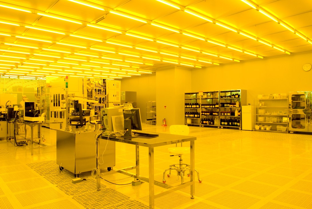 Yellow-lit clean room at KAIST's NanoFab Centre with scientific equipment and storage cabinets.