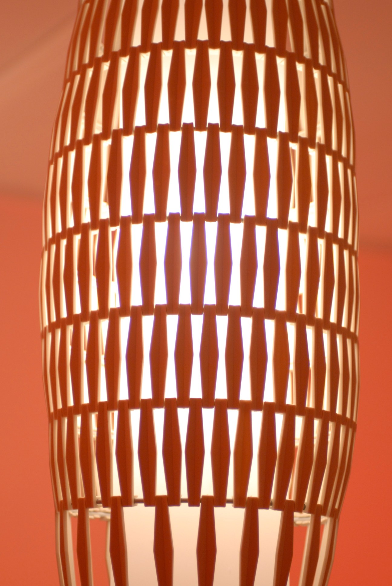 Foscarini 'Tropico' pendant light with orange cylindrical latticed shade glowing against coral background.