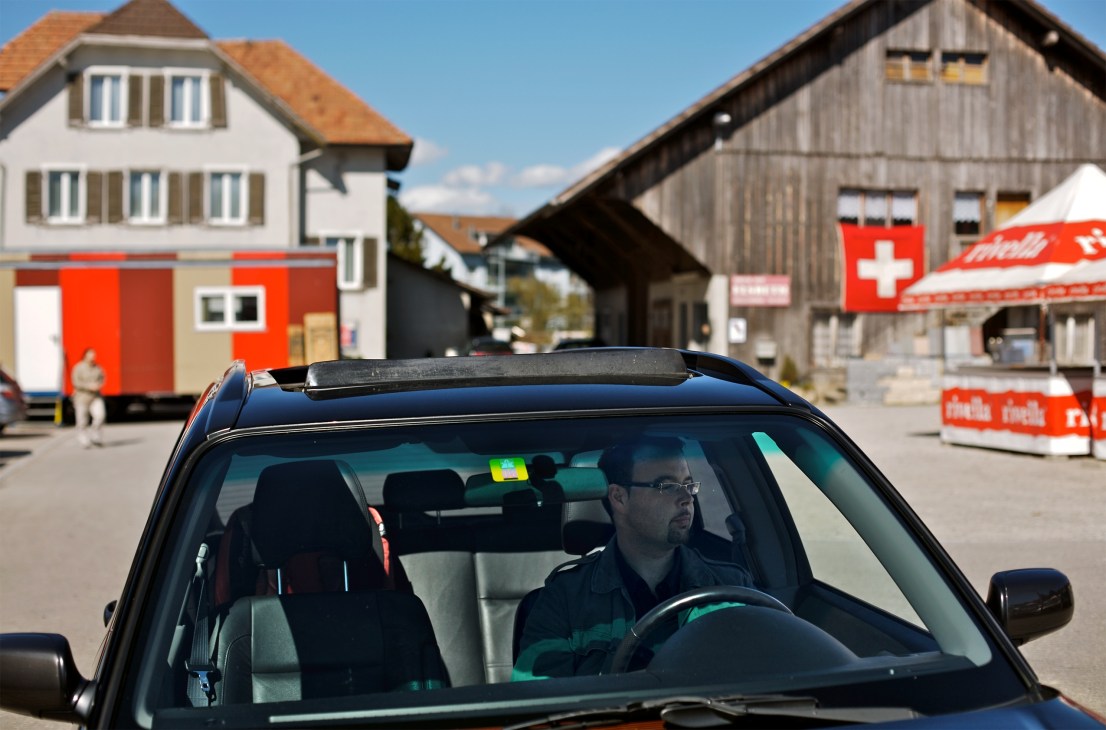 Marco Kölliker sits in his customised blue Subaru Forester XT Turbo in a Swiss village square with Alpine buildings in the background.