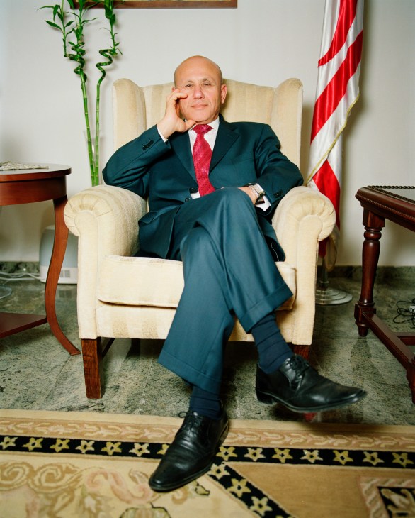 Mehmet Ali Talat sits in a cream armchair in his office, wearing a dark suit and red tie.