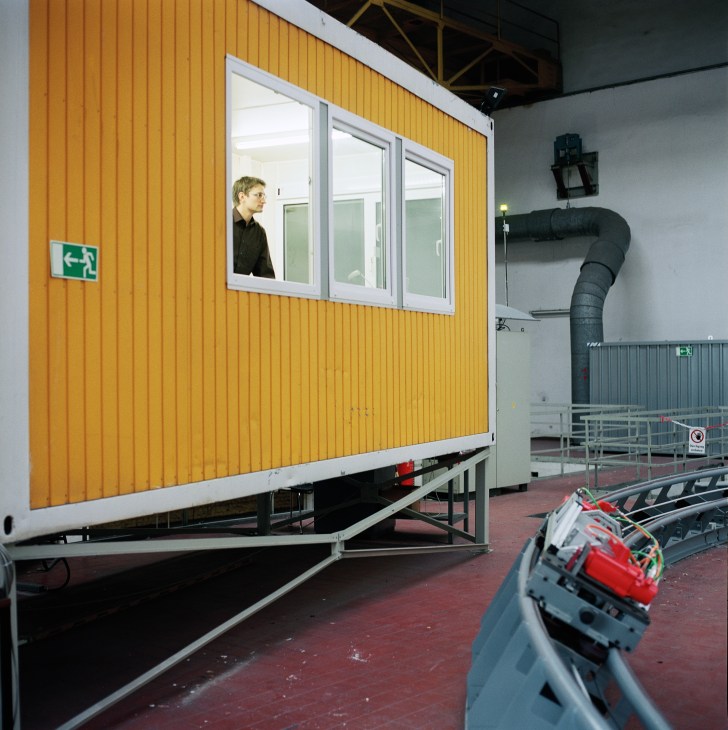 A person sits inside a yellow-walled control cockpit, operating a CargoCap model vehicle on a test track.