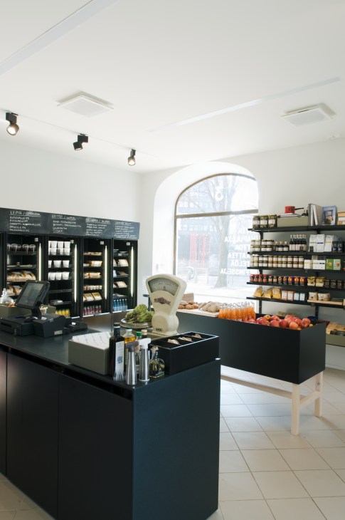 Interior of Sis deli-café with minimalist design, black display cases, shelving with products, and arched window.