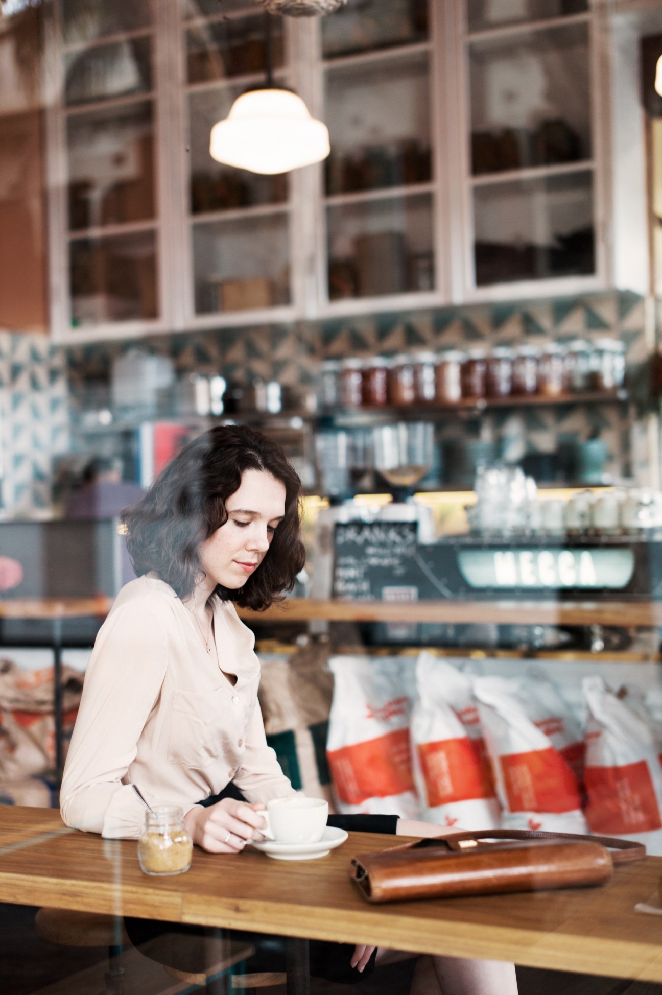 Woman sitting at wooden counter in Brickfields café with coffee cup and pastry display