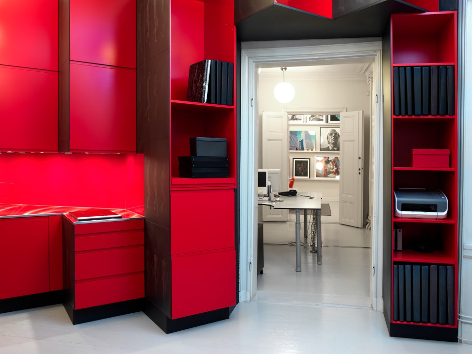 Red lacquered MDF storage wall with black Valchromat panels opens to a bright office space beyond.