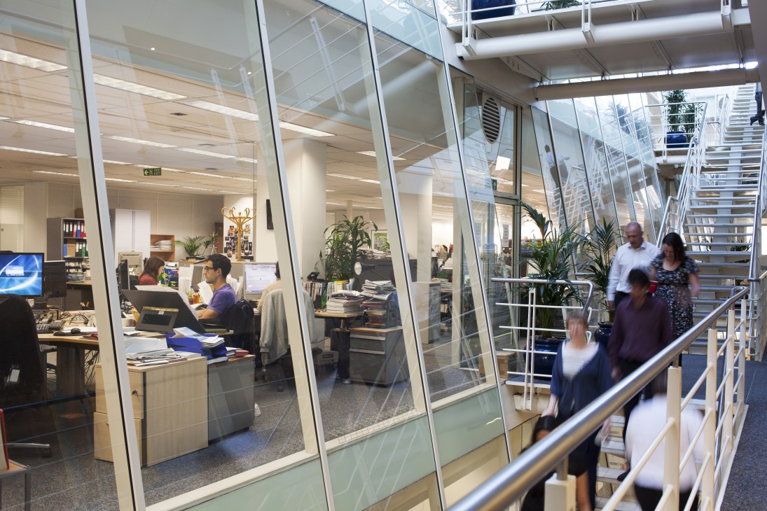 The Lancet editorial floor at Elsevier headquarters showing glass-walled office spaces with staff working at desks and people moving through the modern workplace.